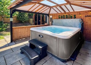 A hot tub with a wooden deck and a bench, surrounded by a wooden fence and a wooden pergola. - The Woldsway (Sauna, Hot Tub & Pet Garden) (Raywell, Beverley)