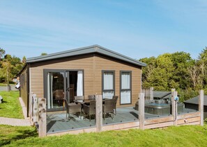 Eine Holzhütte mit einer Terrasse, einem Whirlpool und einem Essbereich mit Stühlen und einem Tisch.