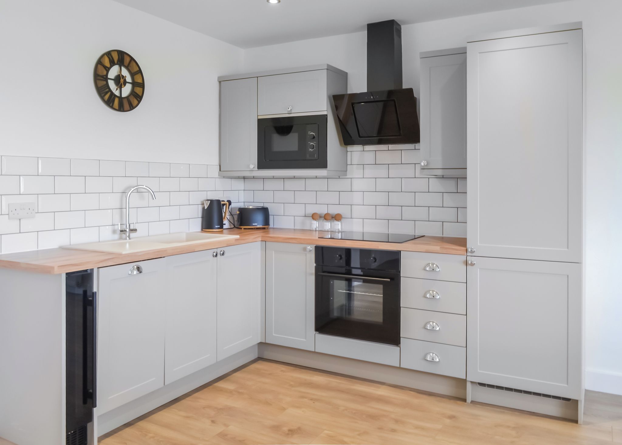 A modern kitchen with white cabinetry, a wooden countertop, a built-in microwave, a stove, and a clock on the wall.