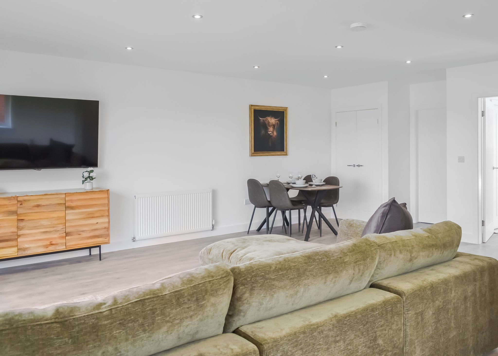 A modern living room with a sofa, a dining table with chairs, a TV mounted on the wall, and a radiator.
