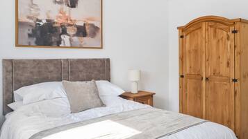 A bedroom with a bed, a nightstand, a lamp, a wooden wardrobe, and a painting on the wall.