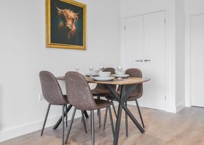 A dining area with a table set for four, chairs, a framed picture on the wall, and a white door in the background. - 1 bedroom accommodation in Hatfield (Hatfield)