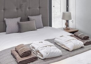 A neatly made bed with a grey headboard, two pillows with a chevron pattern, and a bedside table with a lamp. - Signature Plus 2 Bedroom Lodge Hot Tub (Anstruther)