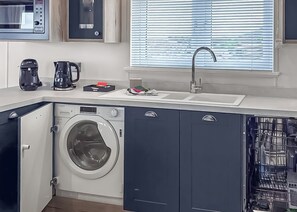 A compact kitchen with a washing machine, coffee maker, and a sink. - Signature Plus2 bedroom lodge hot tub pet friendly (Anstruther)