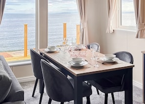 A dining area with a table set for four, a view of the sea, and a window with curtains. - Signature Plus2 bedroom lodge hot tub pet friendly (Anstruther)