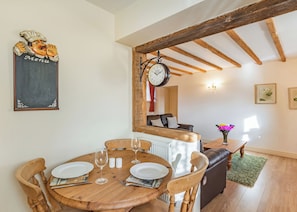 A dining area with a wooden table set for two, a clock, and a wall-mounted menu board. - The Dairy is a charming one-bedroom barn conversion at High Farm Holiday Park. (Beverley)
