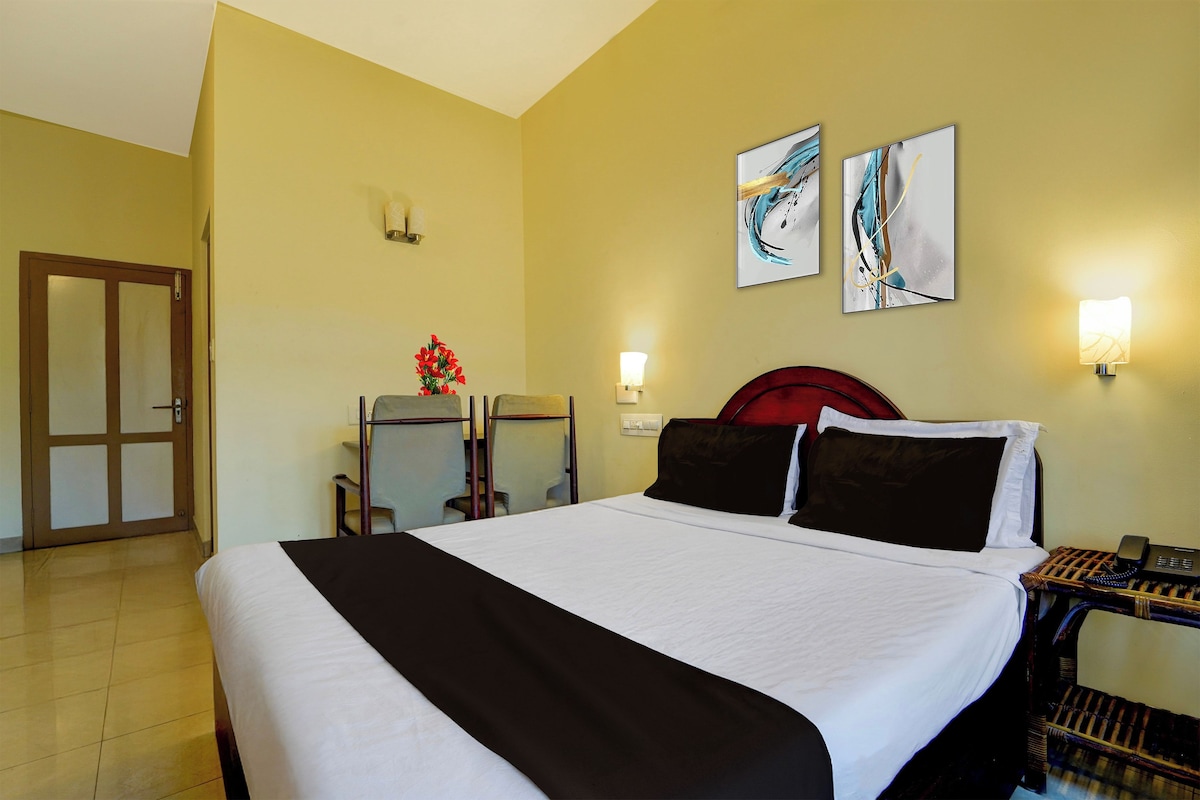 A hotel room with a bed, a desk with a telephone, two wall-mounted lamps, and two abstract paintings.