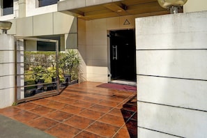 A modern building entrance with a glass door, potted plants, and a tiled floor.