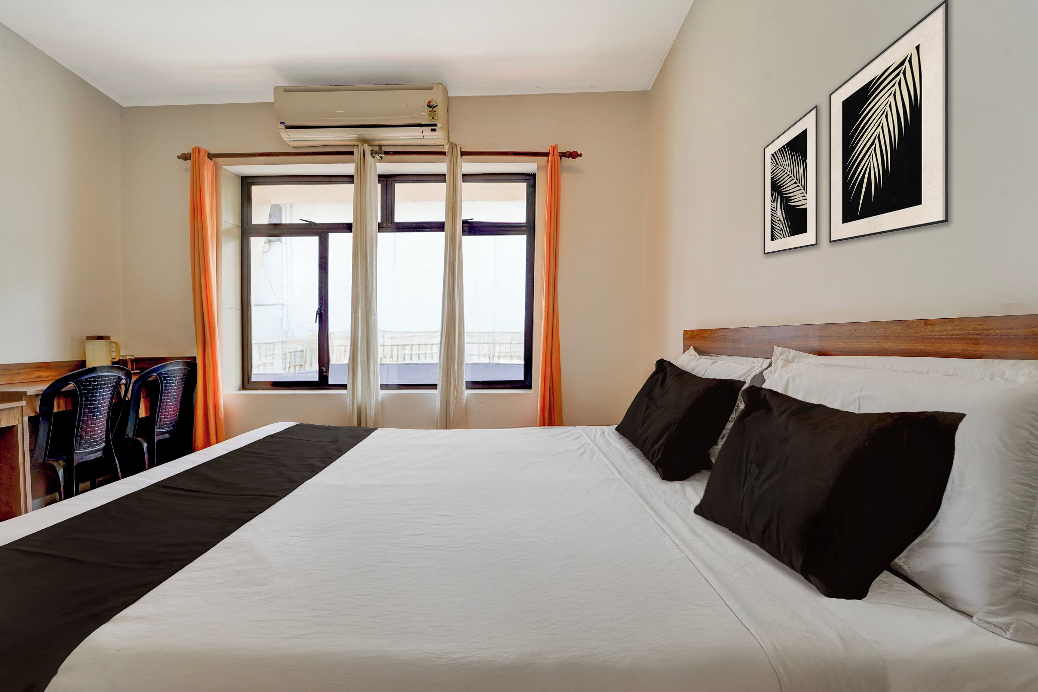 Een hotelkamer met een groot bed, een bureau, twee stoelen, een airconditioning en een raam met gordijnen.