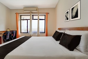 A hotel room with a large bed, a desk, two chairs, an air conditioning unit, and a window with curtains.