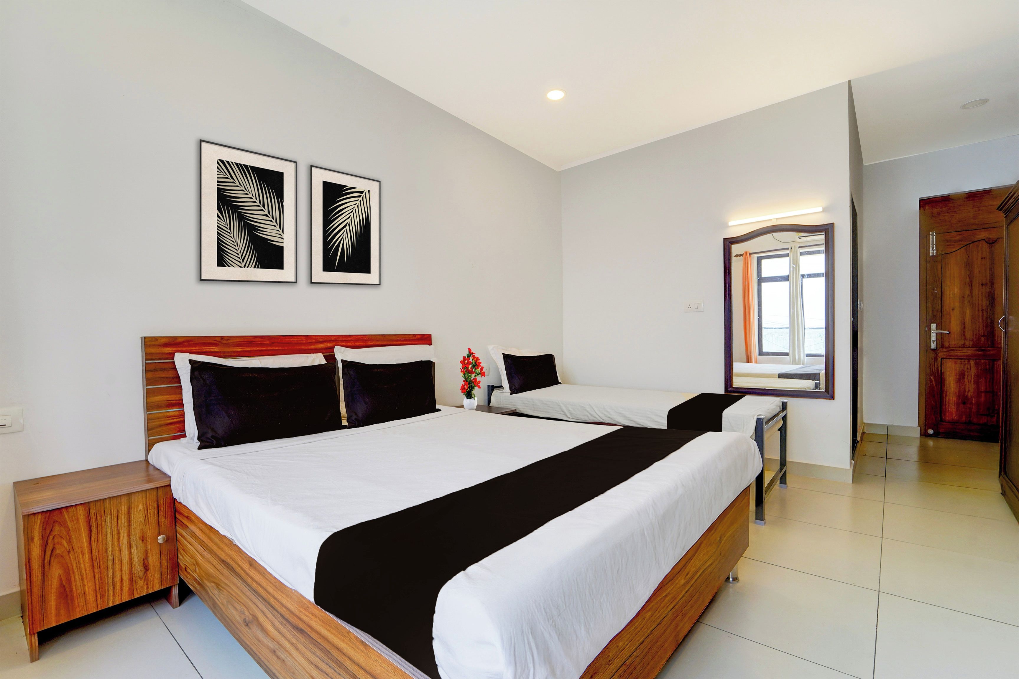 Une chambre d’hôtel avec un grand lit, une table de chevet en bois, un miroir et deux œuvres d’art représentant des feuilles, encadrées et accrochées au mur.