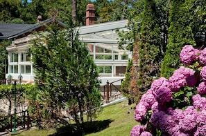 A house with a glass conservatory, surrounded by lush greenery and flowering plants. - Las Cuatro Estaciones (Carilo)