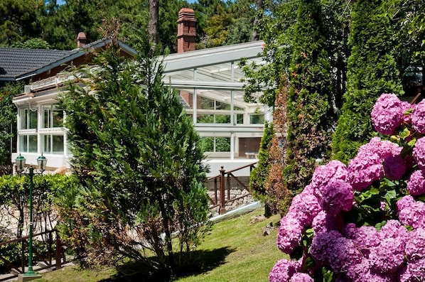 Una casa con un invernadero de vidrio, rodeada de exuberante follaje y plantas en flor.
