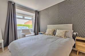 A hotel room with a large bed, a chair, a bedside table, and a view of the outside. - Finest Retreats | Charnwood Forest Lodge (Shepshed)