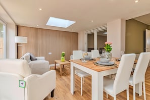 A modern living room with a dining area, featuring a wooden floor, white furniture, and a skylight. - Finest Retreats | Charnwood Forest Lodge (Shepshed)