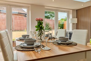A dining area with a wooden table set for four, surrounded by white chairs. - Finest Retreats | Charnwood Forest Lodge (Shepshed)