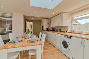 A modern kitchen with a built-in washing machine, a dining area with a table set for four, and a view of the outside. - Finest Retreats | Charnwood Forest Lodge (Shepshed)