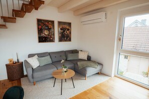 A modern living room with a grey sectional sofa, a round wooden coffee table, and two framed artworks on the wall. - Holiday apartment with 1 bedroom (Eichstetten)
