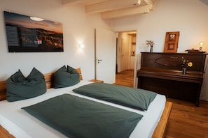 Quarto com cama, almofadas, pintura, cómoda de madeira e porta que dá para outro cômodo.