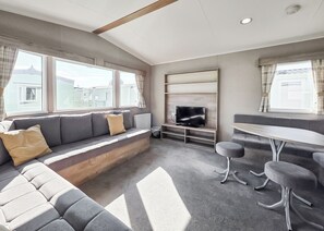A modern living room with a sofa, a TV, and a dining area. - Brand New Luxury Silver Caravan sleeps 8 (Ingoldmells, Skegness)