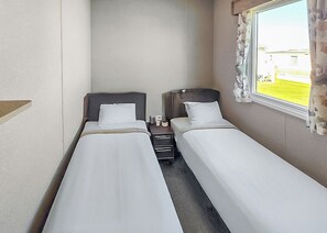 A small, compact room with two single beds, a nightstand, and a window with curtains. - Brand New Luxury Silver Caravan sleeps 8 (Ingoldmells, Skegness)