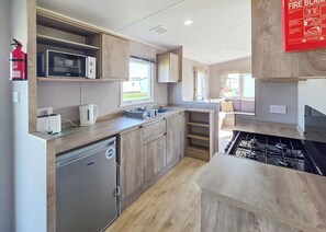 A compact kitchen with a microwave, kettle, sink, and stove. - Brand New Luxury Silver Caravan sleeps 8 (Ingoldmells, Skegness)