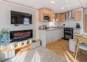 A compact kitchen with a flat-screen TV, microwave, and stove. - The Juniper Platinum is our signature caravan collection. (Dawlish)
