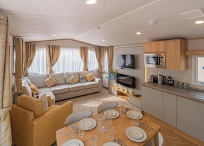 A modern interior with a dining area, sofa, kitchen, and a flat-screen TV. - The Juniper Platinum is our signature caravan collection. (Dawlish)