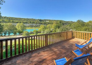A wooden deck with a view of a turquoise lake and green hills. - Hilltop Safari Lodge (Halling)