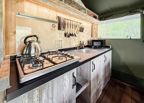 A compact kitchen with a gas stove, a kettle, a microwave, and hanging utensils. - Hilltop Safari Lodge (Halling)