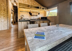 A rustic kitchen with wooden cabinets, a gas stove, and a dining area with a table. - Hilltop Safari Lodge (Halling)