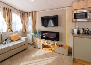 Ett modernt vardagsrum med en platt-TV, en soffa, ett soffbord och en köksdel med en mikrovågsugn.