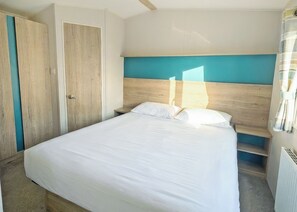 A bedroom with a bed, a wooden wardrobe, and a nightstand. - Platinum 3 bed + Deck (Longridge, Ribble Valley)