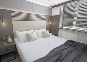 A modern bedroom with a large bed, bedside tables, and a window with blinds. - Autograph S Pod Escape 6 (Hot tub) (Thirsk)