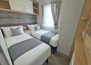 Ein kleines Schlafzimmer mit zwei Betten, einem Kleiderschrank und einem Fenster mit Vorhängen.