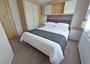 A bedroom with a bed, a wardrobe, a bedside table, and a radiator. - Gold Caravan Sleeps 4 (Roman Bank, Skegness)