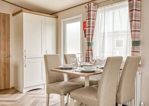 Een eetruimte met een tafel voor vier personen, stoelen, een raam met gordijnen en een witte kast.