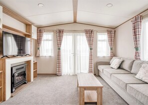 A cozy living room with a fireplace, a sofa, a TV, and plaid curtains. - Kingfisher 2 Bed Hot tub (Pet) (Nr St Austell)