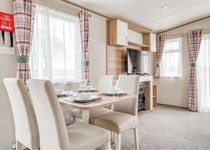 A dining area with a table set for four, chairs, a television, and a fireplace. - Kingfisher 2 Bed Hot tub (Pet) (Nr St Austell)