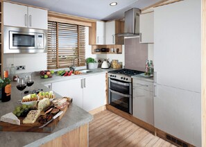 A modern kitchen with stainless steel appliances, wooden cabinets, and a central island with food items. - 1 bedroom accommodation in Nr St Austell (Nr St Austell)