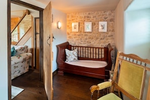 A cozy room with a wooden bench, a sofa with floral upholstery, and a stone wall with framed pictures. - Finest Retreats | Styles Farm Stables (Mappowder)