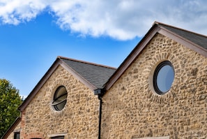A stone building with two circular windows and a sloped roof. - Finest Retreats | Styles Farm Stables (Mappowder)