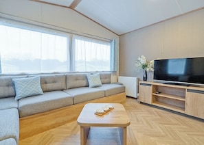 A modern living room with a sectional sofa, a flat-screen TV, and a wooden coffee table. - 1 bedroom accommodation in Dawlish (Dawlish)