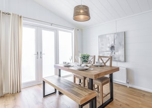 A modern dining area with a wooden table, bench, and pendant lighting. - 1 bedroom accommodation in Westbury (Westbury)