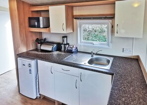A compact kitchenette with a refrigerator, microwave, sink, and window. - Gold Plus 3 No Pets Sleeps 6 Hot Tub (Penhallow)