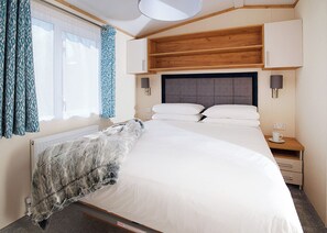 Ein Hotelzimmer mit Bett, Nachttischen, einem Fenster mit Vorhängen und einem Heizkörper.