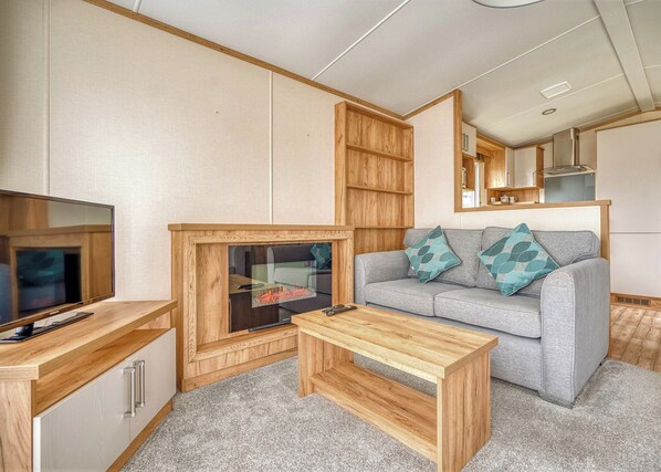 A compact living space with a television, wooden furniture, a sofa with patterned cushions, and a kitchenette. - 1 bedroom accommodation in Nr St Austell (Nr St Austell)