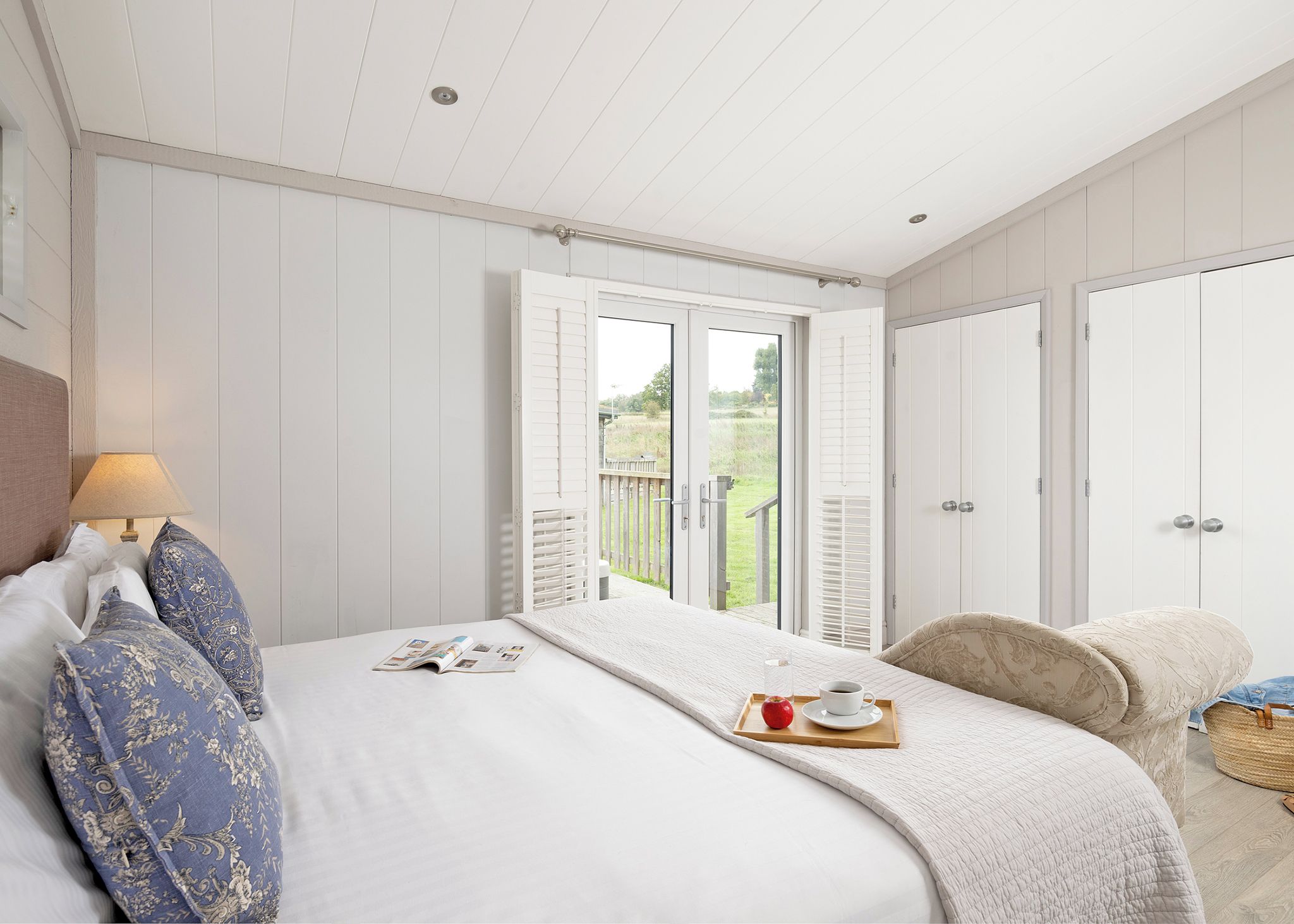 Een slaapkamer met een bed, een nachtkastje met een lamp, een raam met uitzicht op het landschap en een deur.