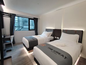 Een hotelkamer met twee bedden, een bureau en uitzicht op buiten.