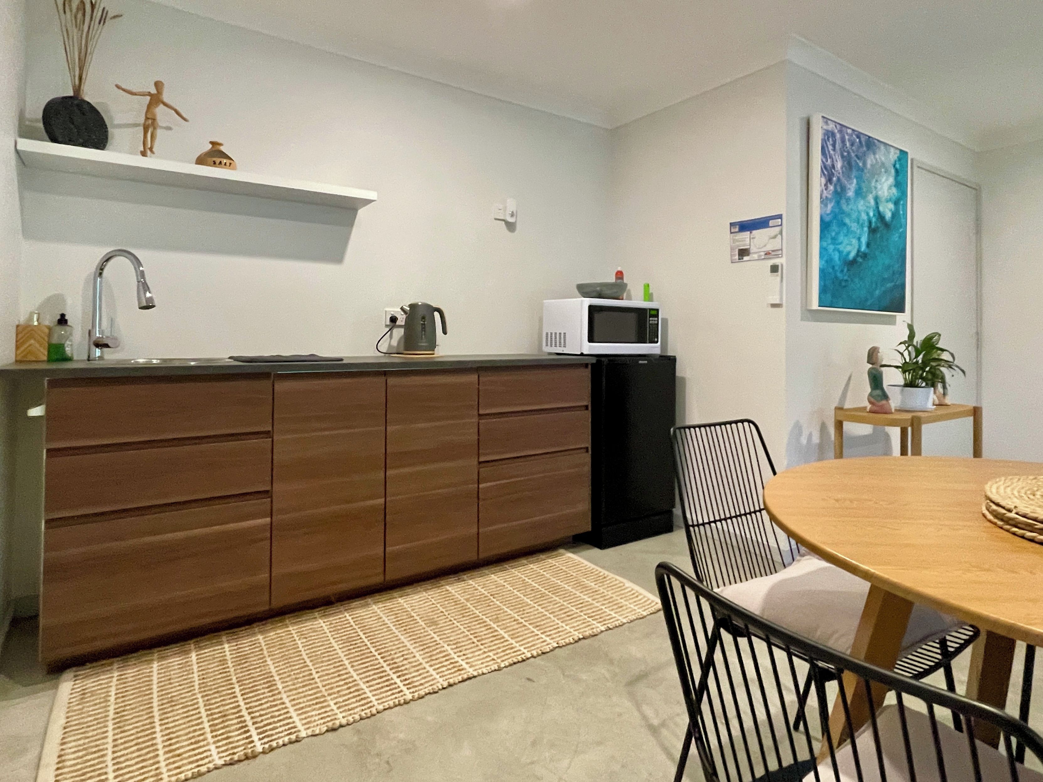 A compact kitchen with a microwave, kettle, and a small sink. There is a dining area with a table and chairs.